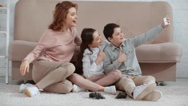 快乐微笑的家庭坐在靠近张子的地毯上，自拍，竖起<strong>大拇指</strong>，和平标志